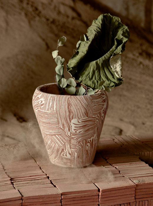 Un vaso di terracotta con decorazioni bianche, che contiene una foglia verde