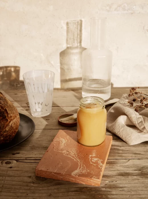 Barattolo di marmellata, bicchiere, caraffe e una noce di cocco su un tavolo di legno