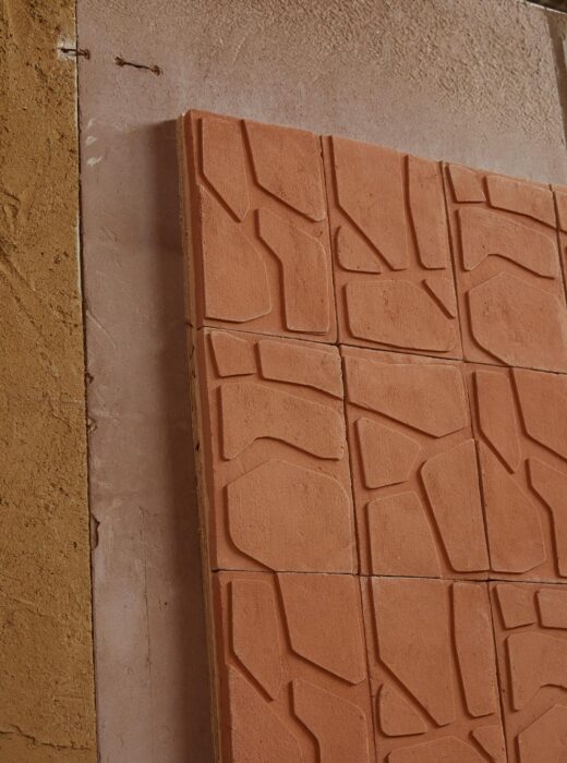 L'immagine mostra un pannello murale composto da piastrelle in terracotta di colore rosso-arancio.