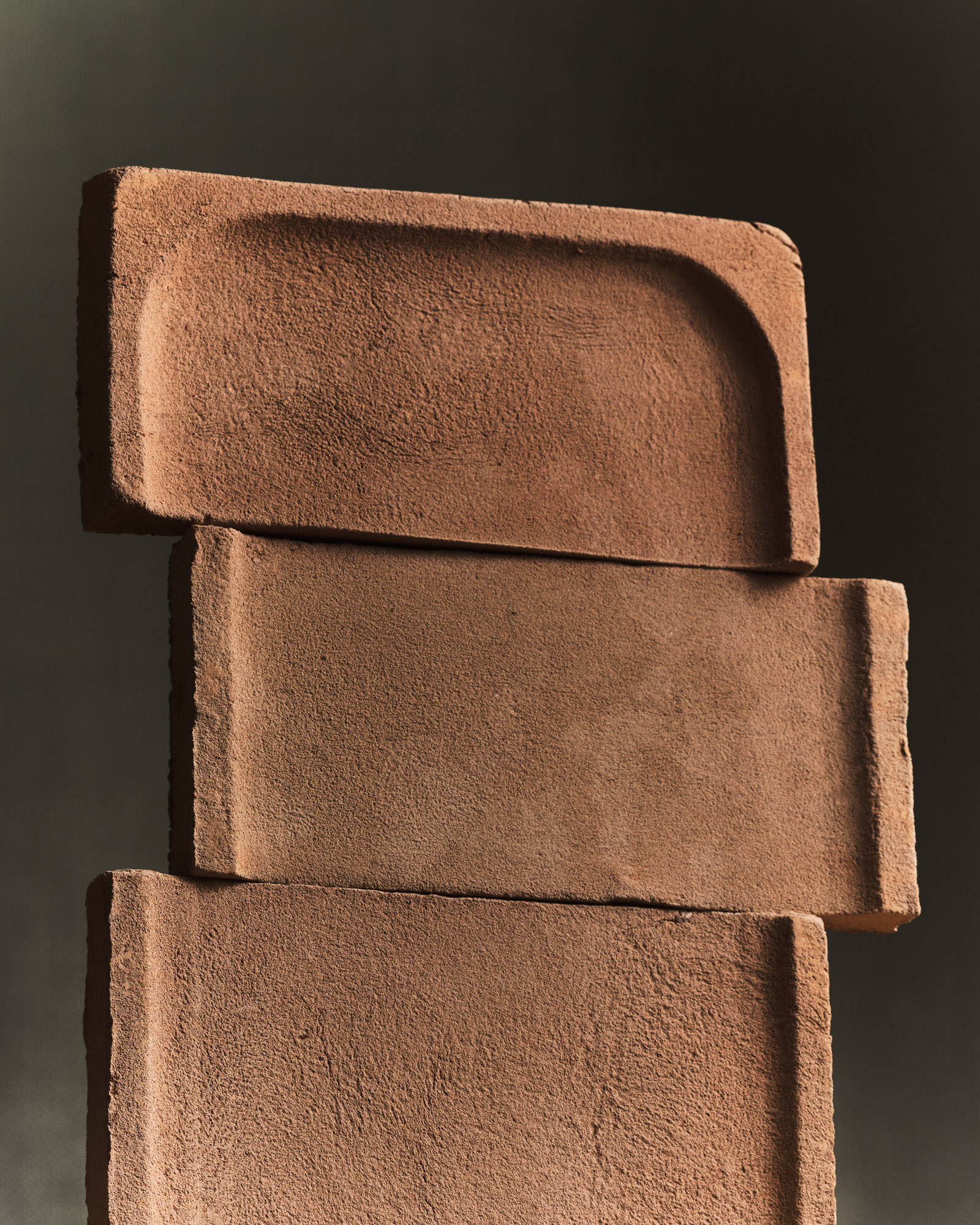 Elementi modulari in terracotta con texture ruvida e forme geometriche sovrapposte su sfondo scuro