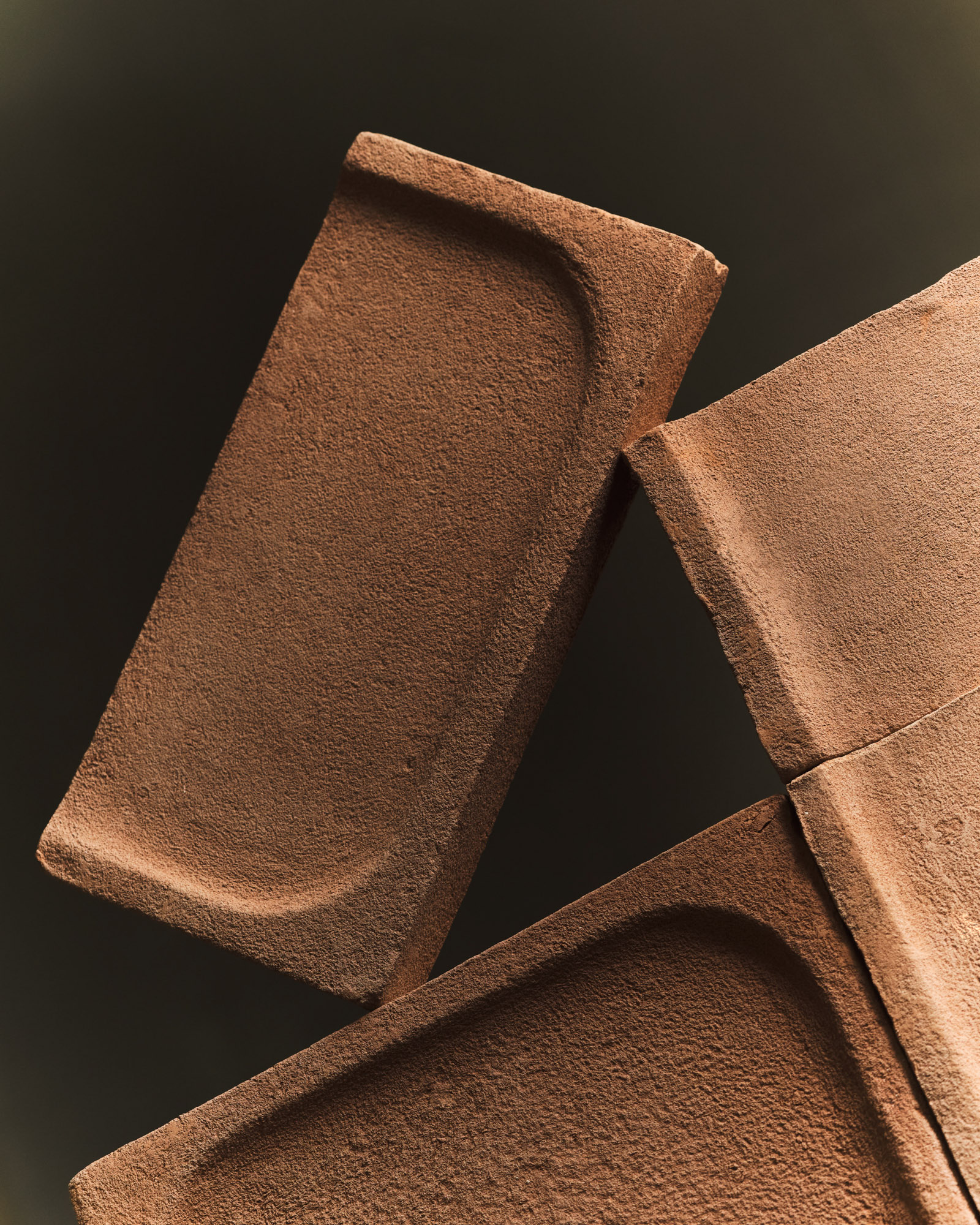 Moduli in terracotta con superfici concave e texture ruvida, disposti in composizione geometrica su sfondo scuro