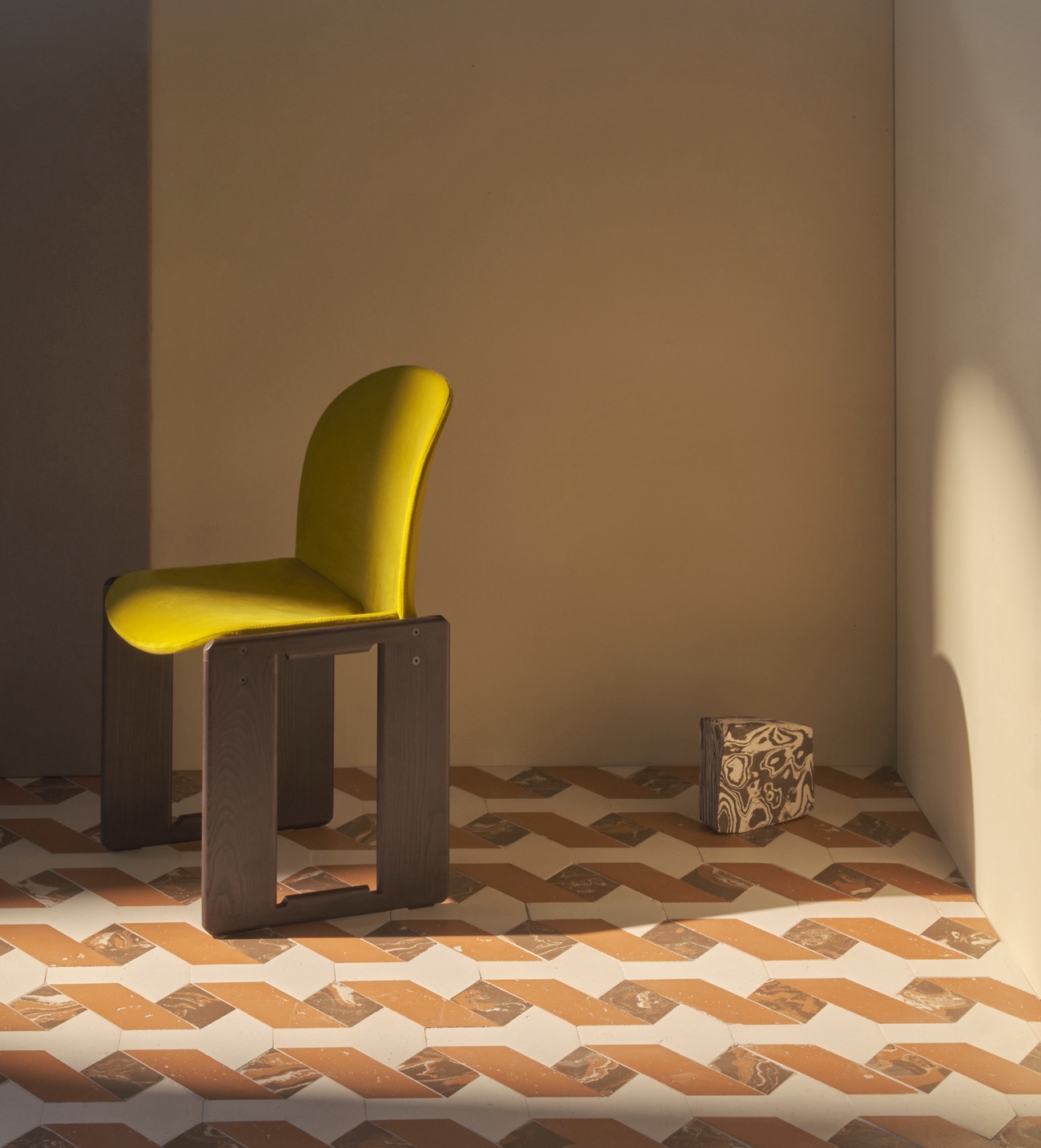 Sedia con seduta gialla su pavimento in terracotta a motivi geometrici, illuminata dalla luce naturale