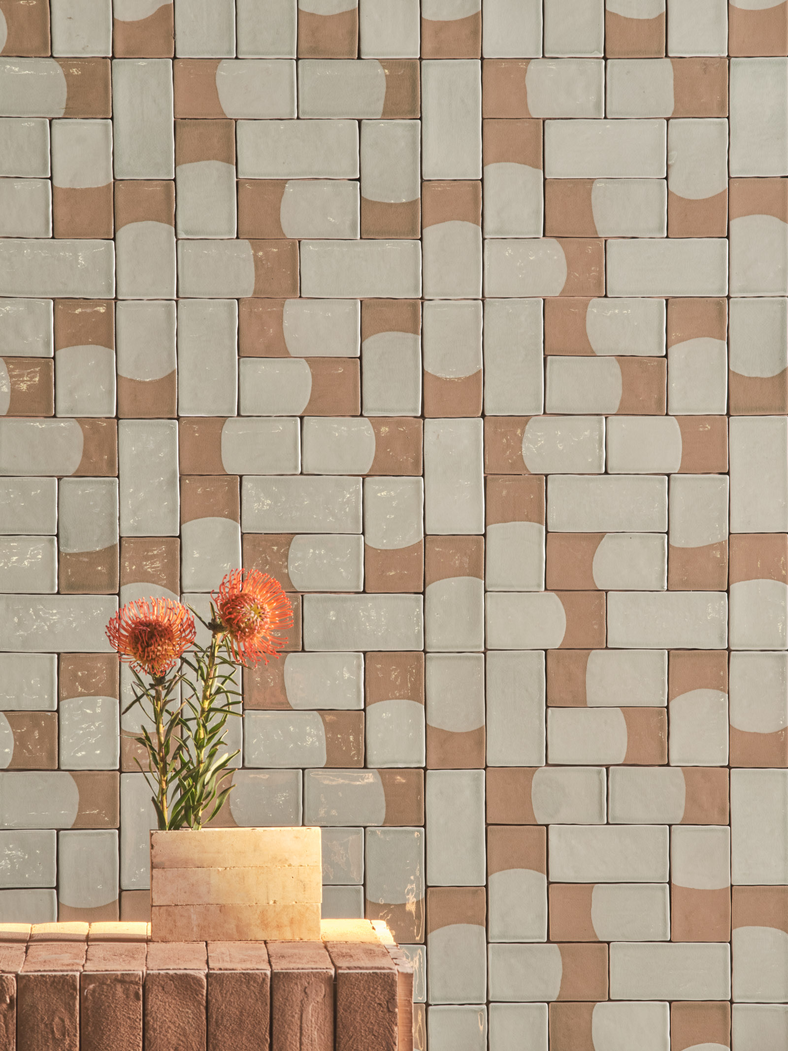 Parete in piastrelle geometriche bicolore con vaso in terracotta e fiori arancioni in primo piano