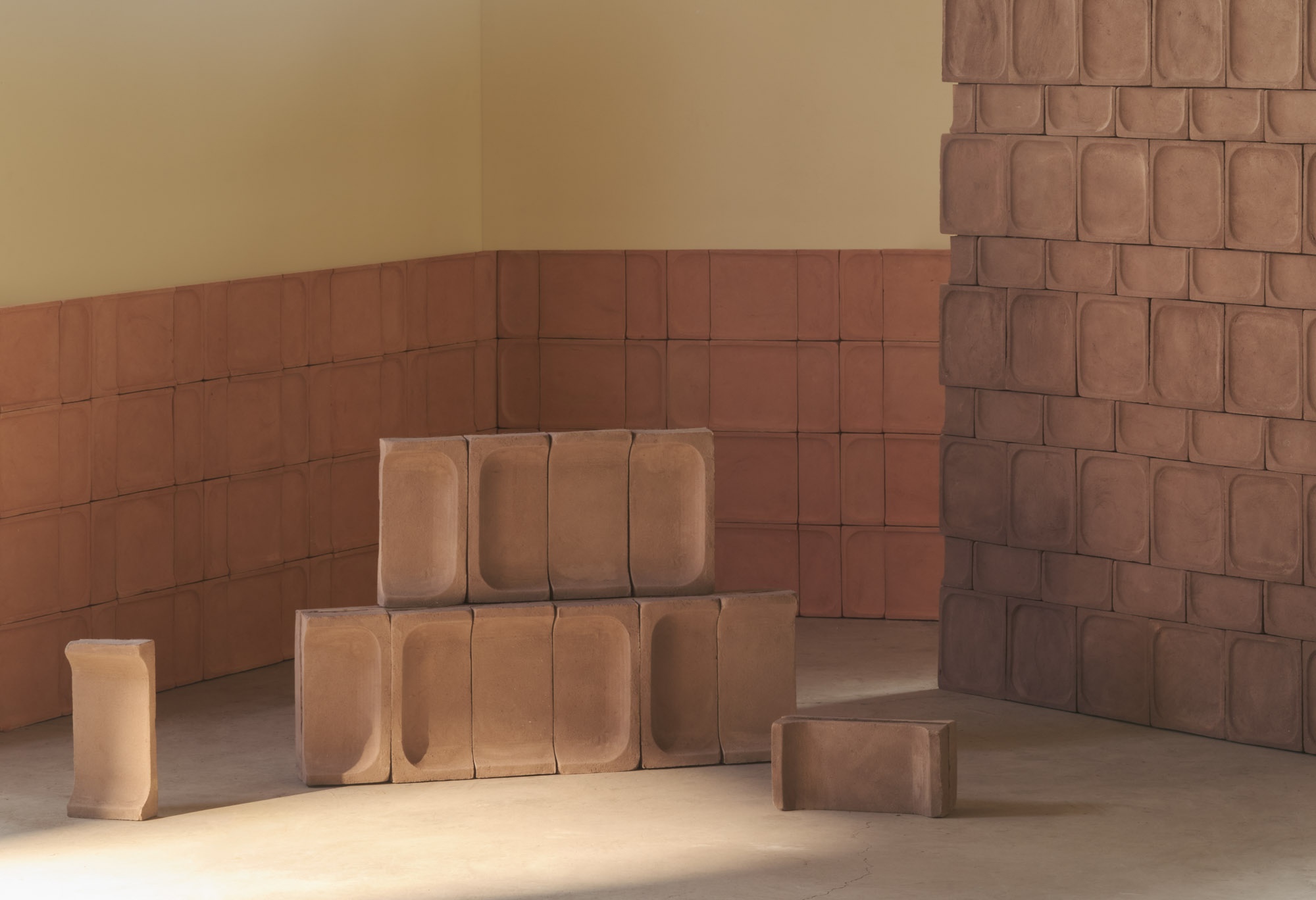 Moduli in terracotta impilati in una stanza con pareti rivestite dello stesso materiale e giochi di luce naturale.