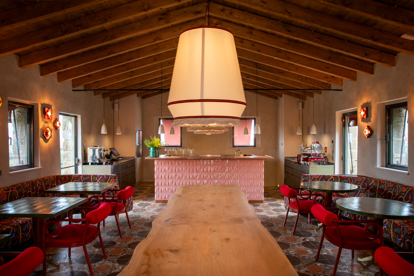 Sala con soffitto in legno, arredi colorati, tavoli in stile rustico e bancone rosa centrale